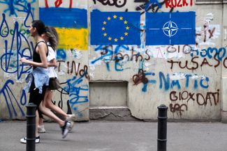 Two women walk past graffiti of the Ukrainian, European Union, and NATO flags in Tbilisi’s old town. May 22, 2023.