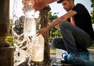 Жители Киева наполняют бутылки питьевой водой из колонки. Отключения электричества, в числе прочего, приводят к перебоям с подачей воды в квартиры. 13 июля 2024 года