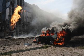 Горящий автомобиль у бизнес-центра в Харькове, поврежденного в результате российского удара 1 сентября 2024 года