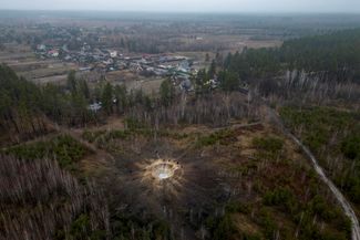 Люди стоят у края воронки, которая образовалась в результате обстрела села Буда-Бабинецкая, расположенного на дороге между Бучей и Бородянкой