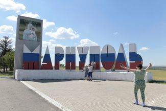 Люди позируют на фоне знака на въезде в Мариуполь. Знак перекрасили в цвета российского флага в июле 2022 года, после того как армия РФ взяла город под контроль