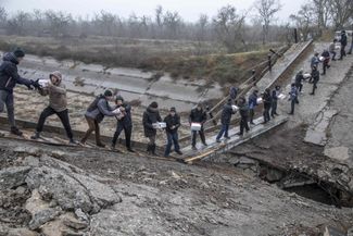 Жители Новопетровки Николаевской области разгружают упаковки с гуманитарной помощью: из-за обрушившегося в результате боевых действий моста автомобиль с ней не может доехать напрямую до села