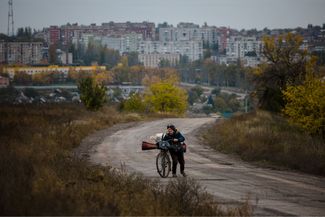 Женщина толкает свой велосипед, нагруженный вещами, на выезде из Бахмута