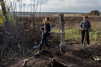 Мальчик с палкой, которую он держит как гранатомет, играет с другом рядом с использованным кассетным боеприпасом в селе Дубовое