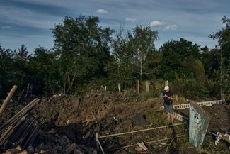 Мужчина смотрит на воронку, возникшую в результате ракетного обстрела на городском кладбище