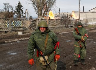 Combatants in pro-Russian militia units patrol Volnovakha’s streets. Behind them, fires fed by broken gas pipes burn.