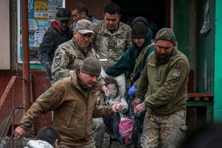 Спасатели выносят ребенка из одного из жилых домов, попавших под обстрел