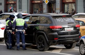 Traffic police officers check the documents of a driver with “No War” written across their car’s back window.