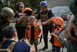 Сотрудники полиции надевают бронежилеты на детей перед эвакуацией из Степногорска, расположенного недалеко от линии фронта 