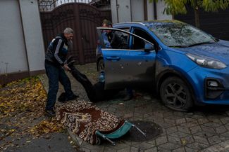 Сотрудники городской службы уносят тело женщины, погибшей в своей машине во время обстрела