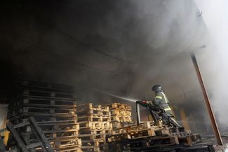 Пожарный тушит огонь на складе, возникший в результате обстрела. 