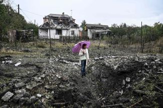 Женщина смотрит на громадную воронку после российского обстрела, позади полуразрушеный жилой дом. «Краматорск обстреливают авиацией и ракетами, только за вчера было больше шести ракет», — рассказал в понедельник мэр города Александр Гончаренко