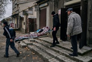 Местные жители выносят тело 20-летнего мужчины, погибшего в ходе обстрела